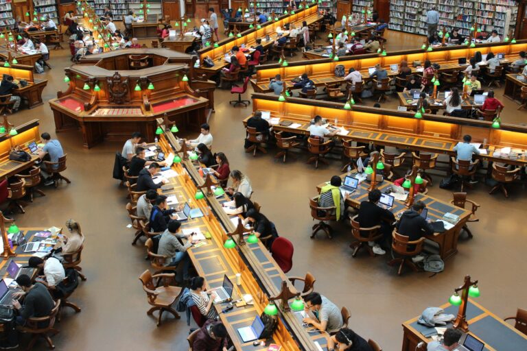 A lively university library scene with students studying diligently at wooden desks. ZANN Consultants